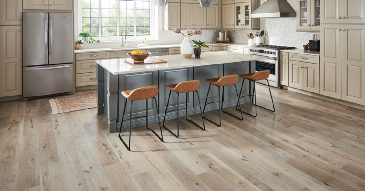 Large kitchen with an island, white marble countertops, light blue cabinets, four brown stools, a beige luxury vinyl floor